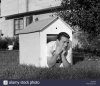 1960s-man-in-doghouse-in-backyard-resting-on-elbows-with-frown-on-CMT3P8.jpg